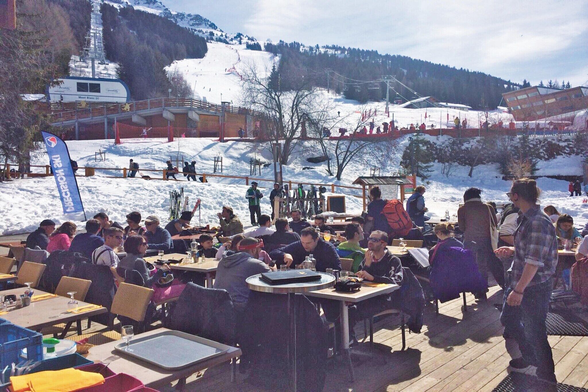 Un espace repas avec des tables et des chaises, un télésiège en arrière-plan et un paysage montagneux.
