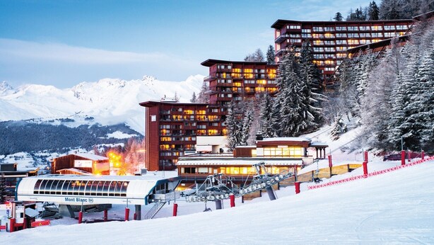 Ein modernes Skiresort mit mehreren Gebäuden, einer Seilbahn und schneebedeckten Bäumen.