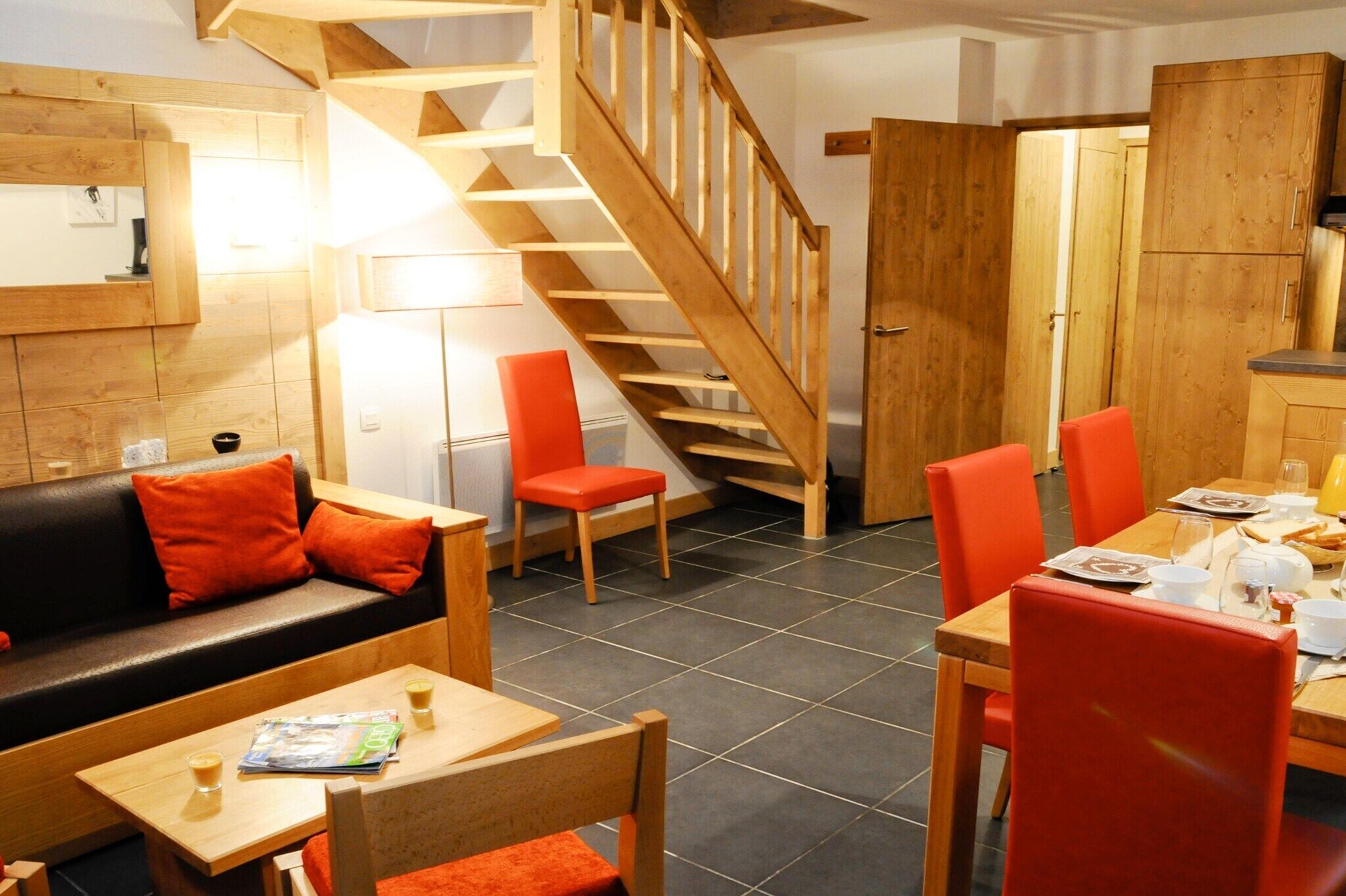 Ein modernes Interieur mit einer Holztreppe, einem Essbereich mit roten Stühlen und einem Sofa mit orangefarbenen Kissen.