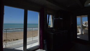 A room with a large sliding glass door leading to a beach view, a kitchen area with a sink and cabinets, and a balcony with a railing. - Appartamento Tramonto sul Mare (Caucana)