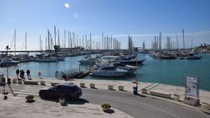 A marina with numerous boats docked, a pedestrian walkway, and a car parked on the side. - Appartamento Tramonto sul Mare (Caucana)