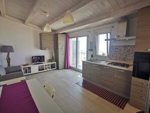Eine moderne Küche mit einer zentralen Kochinsel, ein Essbereich mit Tisch und Stühlen sowie ein Wohnbereich mit Sofa und Fernseher.