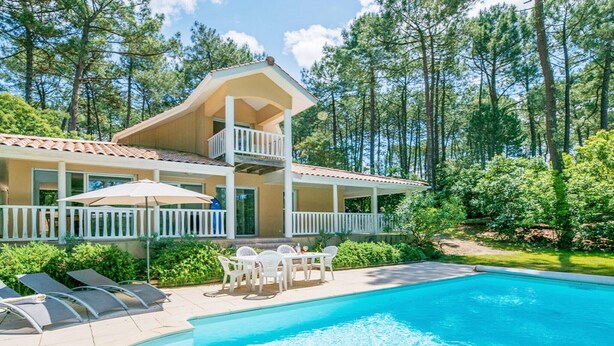 Une maison à deux étages avec une piscine, un balcon et une terrasse équipée de chaises et de parasols.