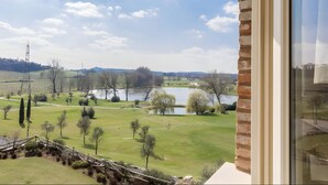 Vista da janela com área gramada, árvores, lago e colinas ao longe.