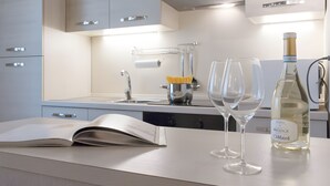Uma cozinha moderna com bancada branca, um livro, duas taças de vinho e uma garrafa de vinho.