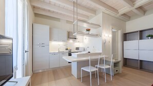 Cozinha moderna com armários brancos, uma ilha central e uma área de jantar com cadeiras brancas.