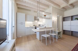 A modern kitchen with white cabinetry, a central island, and a dining area with white chairs. - Chervo Golf Apartment Two (Lombardia)