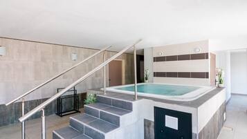 A modern indoor pool area with a staircase leading to a hot tub, surrounded by neutral-toned walls and minimalistic decor.