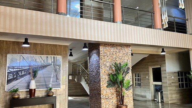 Um hall amplo com teto alto, escada e uma grande moldura com a imagem de uma ponte.