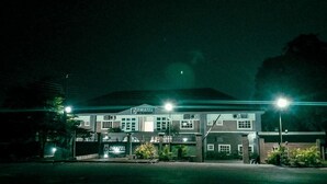 Um motel à noite com uma placa 'DMATEL HOTEL RESORT', apresentando um prédio de dois andares com várias janelas e telhado plano.