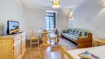 Una habitación con una cama de madera, una mesa de madera con sillas, un sofá, un televisor sobre un mueble de madera y una ventana con cortinas.