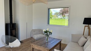 A modern living room with a wood-burning stove, a dining table with a vase of flowers, a grey armchair, and a sofa. - New wooden house less than 5 minutes from the beach (Gouville-sur-Mer)