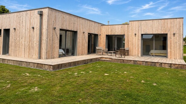 A modern wooden house with large sliding glass doors, a deck, and a grassy yard. - New wooden house less than 5 minutes from the beach (Gouville-sur-Mer)