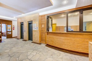 Un espace d’accueil doté d’un comptoir de réception en bois, de deux ascenseurs et d’un sol carrelé en pierre.