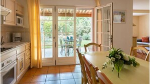 Eine Küche mit Essbereich, einem Tisch mit Stühlen, einer Blumenkomposition und Blick durch Glastüren.