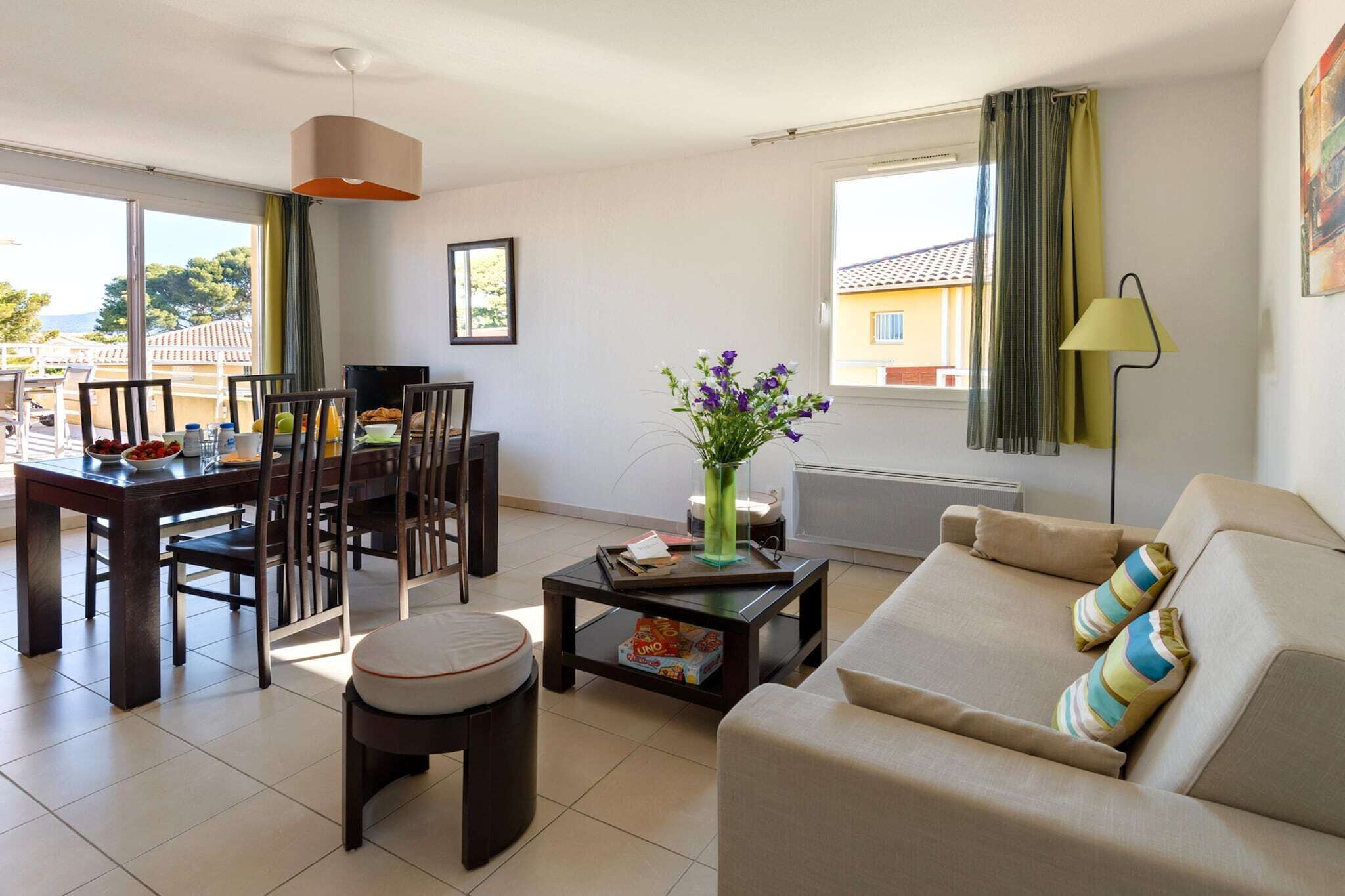A modern living room with a dining area, a sofa, a coffee table, and a view of the outside.