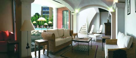 A spacious living area with a sofa, armchairs, and a coffee table, featuring a view of an outdoor pool area.