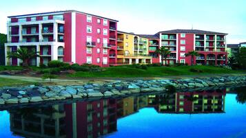 Um hotel com vários andares, varandas, piscina e reflexo na água.