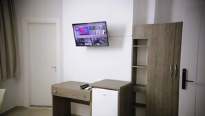 A compact room with a desk, a television mounted on the wall, a wardrobe, and a small refrigerator. - Alv Rent Room (Vlorë)