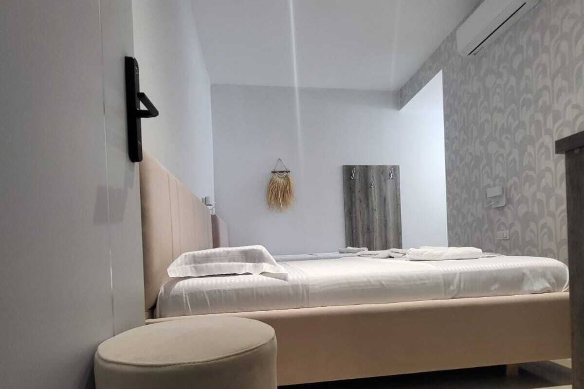 A modern bedroom with a bed, a round ottoman, a wall-mounted number, and a patterned wall.