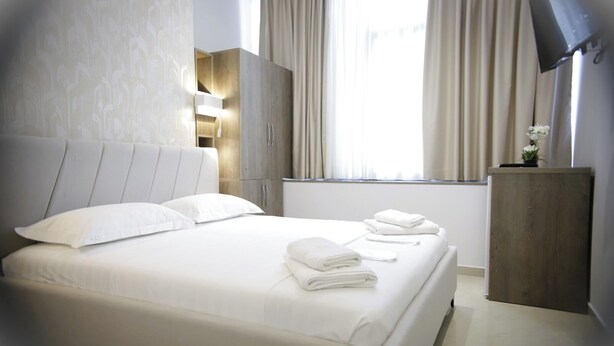 A hotel room with a large bed, a wooden wardrobe, a desk with a lamp, and a TV on the wall. - Alv Rent Room (Vlorë)