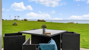 An outdoor seating area with wicker furniture, a table, and a view of the sea. - Sct. Knudsborg · Cottage 12H · Sea view (Middelfart)