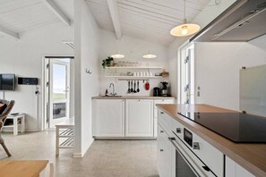 Eine moderne Küche mit weißen Schränken, einer Holz Arbeitsplatte und einem eingebauten Backofen. Es gibt einen Essbereich mit Tisch und Stühlen sowie einen an der Wand montierten Fernseher.