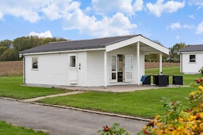 Ein kleines, eingeschossiges Mobilheim mit überdachter Veranda, einer kleinen angebauten Garage und einem Rasengrundstück.