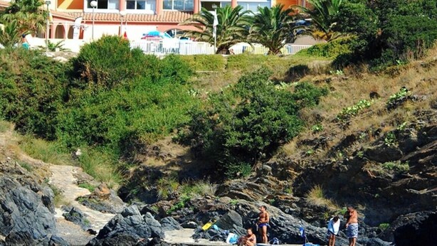 Un edificio frente al mar con varios balcones, una piscina y un litoral rocoso.