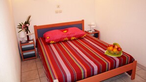 A bed with a striped bedspread, a red pillow, a bedside table with a lamp, and a fruit basket on the bed. - Family duplex with patio (Saint-Cyprien)