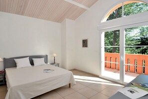 A bedroom with a bed, a nightstand, a lamp, a window with a view of a brick wall and trees.