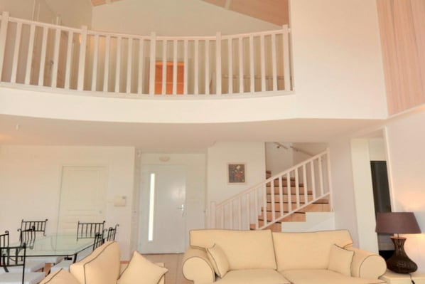 A living room with a glass dining table, a beige sofa, a staircase, and a white railing.