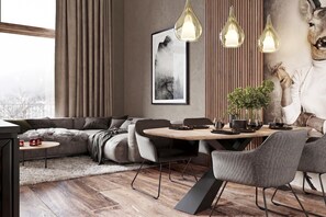 Ein modernes Wohnzimmer mit einer Couch, einem Esstisch, Stühlen, Pendelleuchten, einem gerahmten Bild und einem dekorativen Hirschkopf.