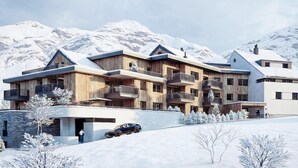 A modern multi-story building with balconies, set against a snowy mountain backdrop.