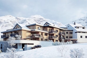 Ein modernes mehrgeschossiges Gebäude mit Balkonen vor einer verschneiten Berglandschaft.
