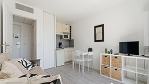 Ett kompakt bostadsutrymme med ett litet kök, en matplats, en TV och förvaringslådor.