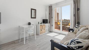 A modern living room with a sofa, a TV, a small white table, and a balcony with a view.