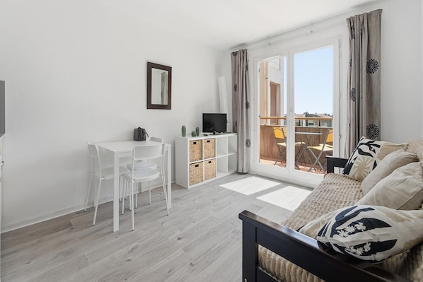 Ein modernes Wohnzimmer mit Sofa, Fernseher, einem kleinen weißen Tisch und einem Balkon mit Blick.