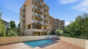 En flervåningsbostadsbyggnad med balkonger, en swimmingpool och omgivande grönska.