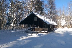 Eine Holzhütte mit schneebedecktem Dach, umgeben von Bäumen in einer verschneiten Landschaft.