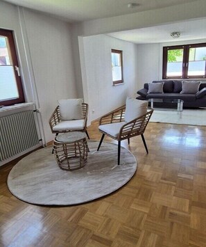 Ein Wohnzimmer mit einem runden Tisch, zwei Korbstühlen, einer Couch und einer Heizung.
