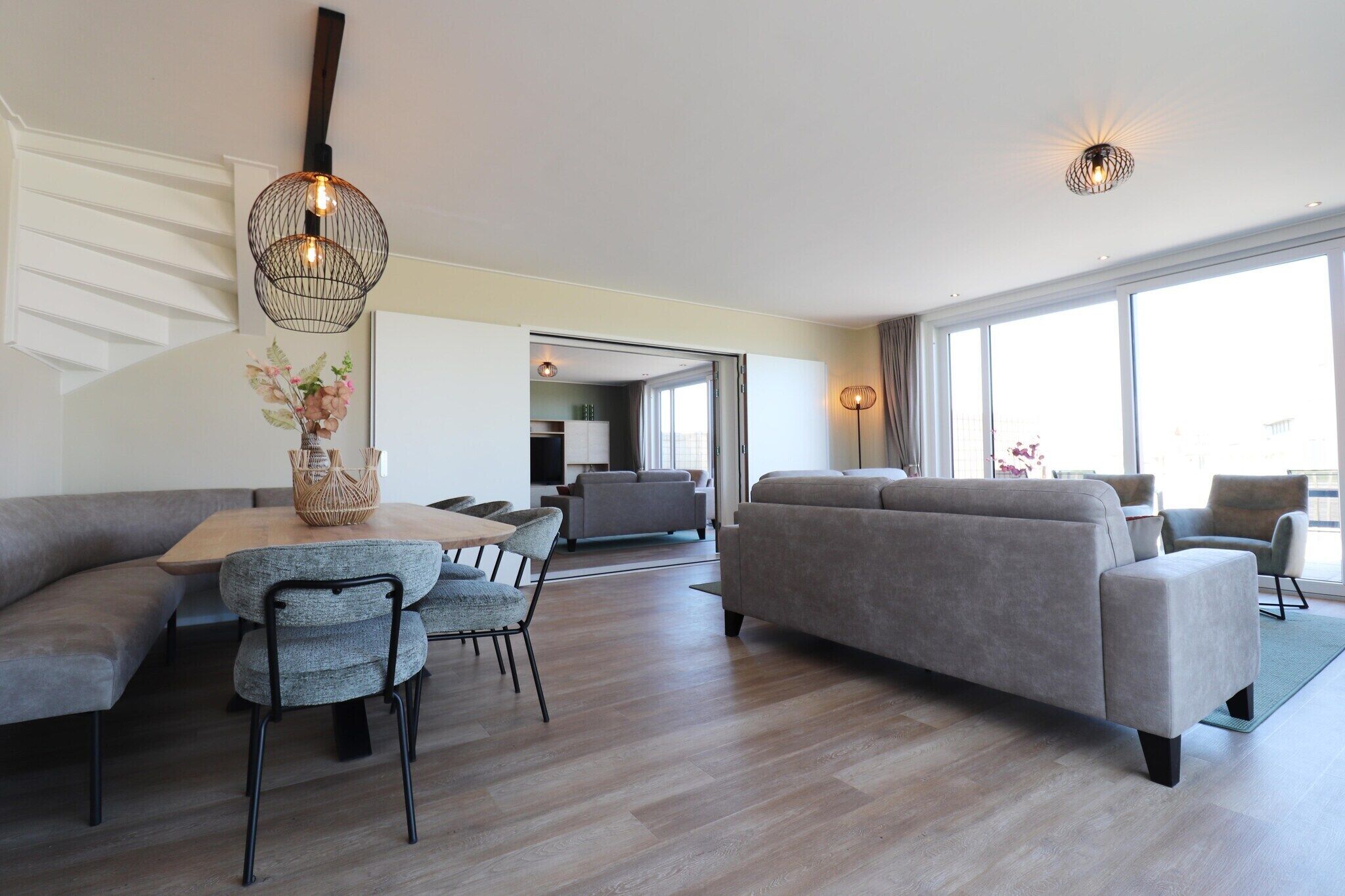 A modern living room with a sofa, dining table, chairs, and a hanging light fixture.
