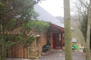 A rustic wooden building with a red door, a covered porch, and a gravel driveway. - Holiday home in the meadows (Kall)