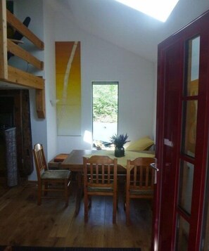 A dining area with wooden furniture, a window, and a red door. - Holiday home in the meadows (Kall)