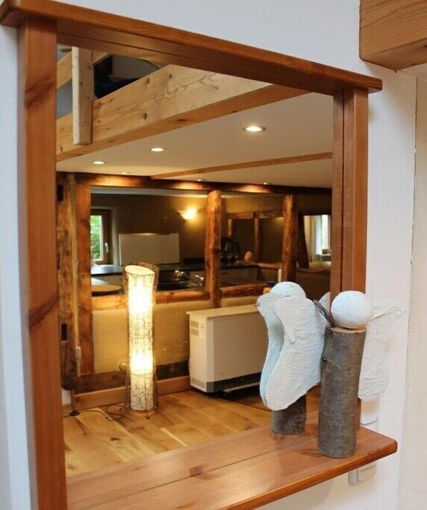 A wooden-framed mirror reflecting a kitchen area with a refrigerator, a lamp, and a towel rack. - Holiday home in the meadows (Kall)