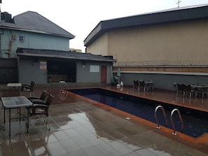 An outdoor swimming pool with a tiled deck, surrounded by tables and chairs. - Dmatel Gold Hotel (Port Harcourt)