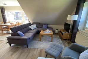 Een woonkamer met een hoekbank, een bijzettafeltje, een televisie en een lamp.