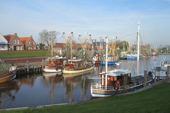 A marina with several fishing boats docked, a lock system, and residential buildings in the background. - Holiday apartment in Greetsiel with Wi-Fi (Greetsiel)
