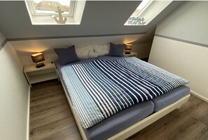Een slaapkamer met dakraam, een bed met gestreepte lakens, twee bedlampen en een nachtkastje.