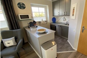 A compact kitchen with a microwave, a sink, and a small island with a bowl. - Holiday apartment in Greetsiel with Wi-Fi (Greetsiel)